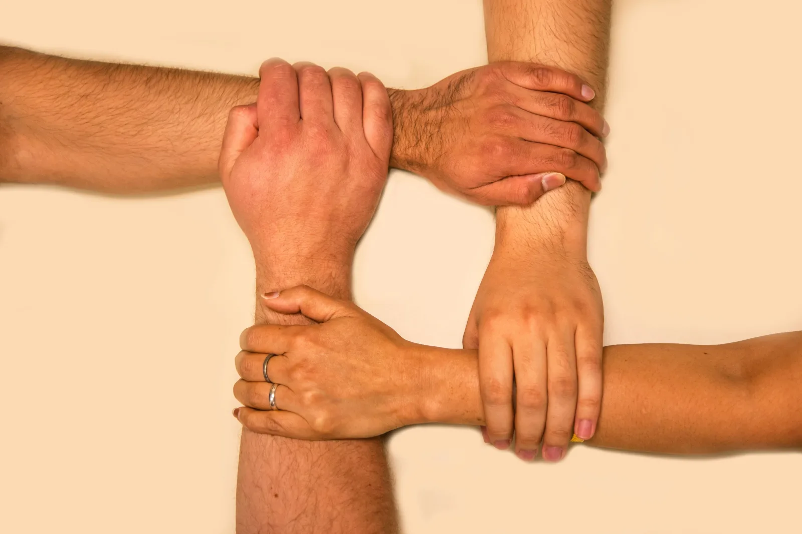 4 pessoas apoiando a mão no pulso de cada um indicando cooperação